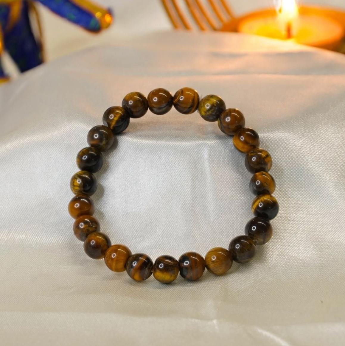 Tiger eye beaded bracelet on a white fabric background with a candle in the background